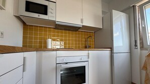 Cuina compacta amb armaris blancs, microones, forn i nevera.