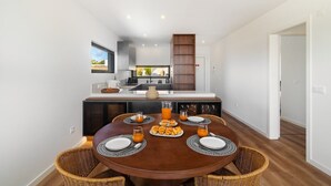 Un coin repas moderne avec une table ronde, des chaises en osier et une table préparée pour le petit-déjeuner avec des croissants et du jus d’orange.