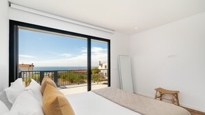 Une chambre avec un grand lit, une vue sur la mer et un balcon aménagé avec du mobilier d’extérieur.