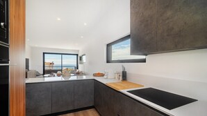 Une cuisine moderne dotée d’un grand îlot central, de meubles de rangement aux couleurs sombres et offrant une vue sur l’extérieur.