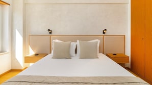 A bedroom with a large bed, two bedside tables, a wooden wardrobe, and a window providing natural light. - Modern Apartment with Great Atmosphere (Lisbon)