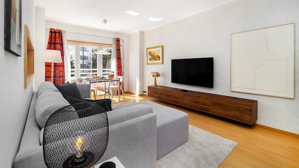 A modern living room with a grey sectional sofa, a flat-screen TV, and a wooden cabinet. - Modern Apartment with Great Atmosphere (Lisbon)