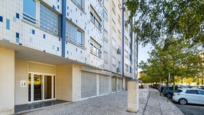 A building with a tiled facade, a covered entrance, and parked cars along the street. - Modern Apartment with Great Atmosphere (Lisbon)