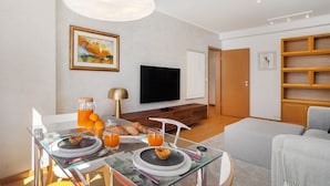 A modern living room with a glass dining table set for breakfast, a flat-screen TV, and a bookshelf. - Modern Apartment with Great Atmosphere (Lisbon)