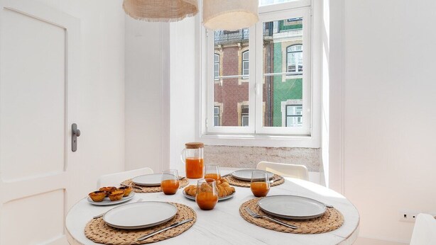 Mesa redonda de comedor con platos, cubiertos y vasos preparados para el desayuno.