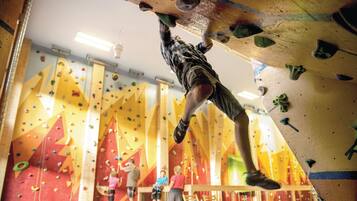 A person climbing a rock wall indoors with various holds and a wooden floor below.