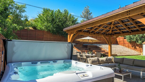 Un jacuzzi bajo una pérgola de madera, con mobiliario de exterior y una zona de terraza.