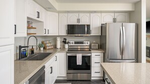 Una cocina moderna con armarios blancos, electrodomésticos de acero inoxidable, encimera de granito y horno empotrado.