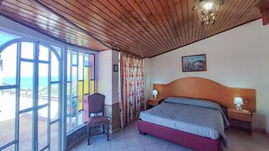 A bedroom with a bed, a chair, a nightstand, a lamp, a picture on the wall, and a view of the sea through large windows. - Nice home in Gioiosa Marea (Gioiosa Marea)