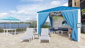 Ein überdachter Außenbereich mit Blick auf den Pool, ausgestattet mit einer Laube, Liegestühlen und Sonnenschirmen.
