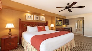 Ein Hotelzimmer mit einem großen Bett, zwei Nachttischlampen, einem Deckenventilator, einer kleinen Küchenzeile und einem durch eine geöffnete Tür einsehbaren Badezimmer.