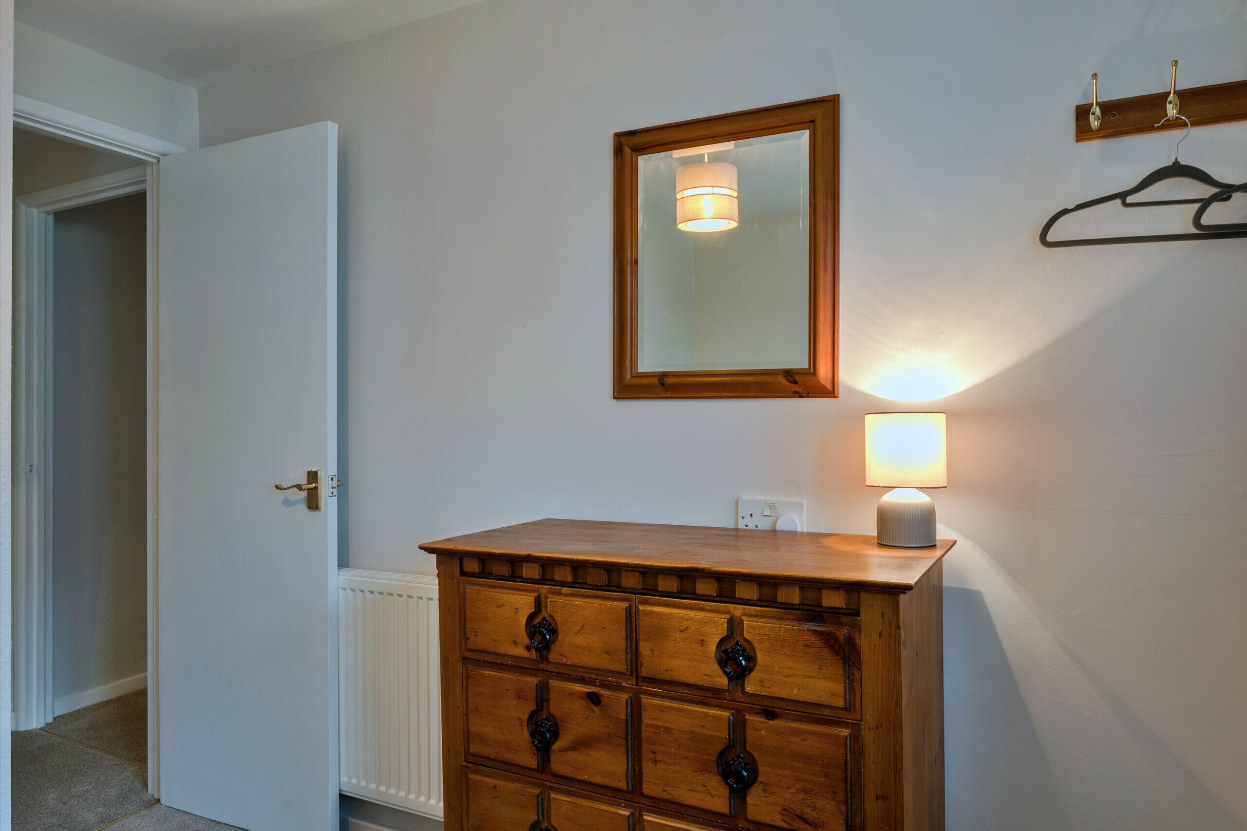 Een houten dressoir met lades, een spiegel erboven en een wandlamp.