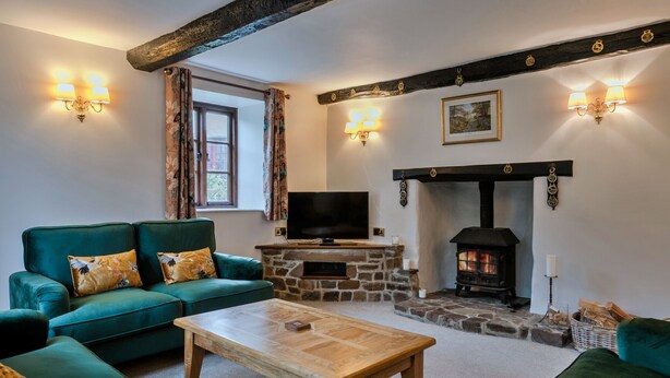 A cozy living room with a stone fireplace, green sofas, a wooden coffee table, and a television.