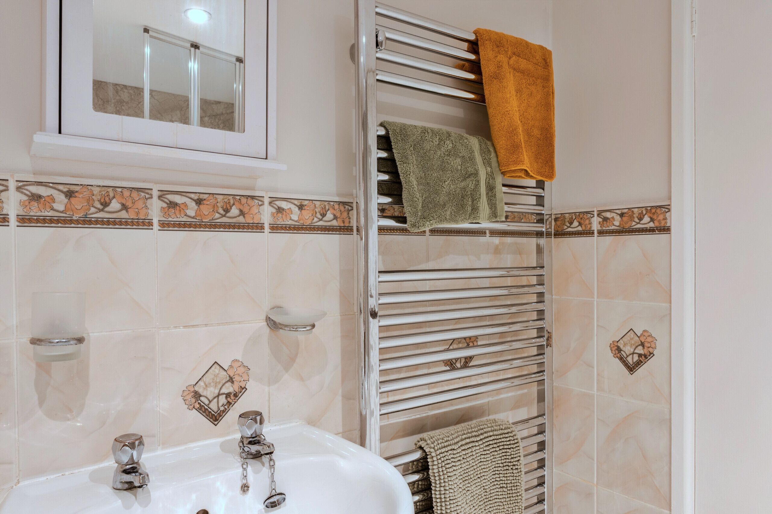 Een badkamer met een wastafel, spiegel, handdoekrek en decoratieve tegels.