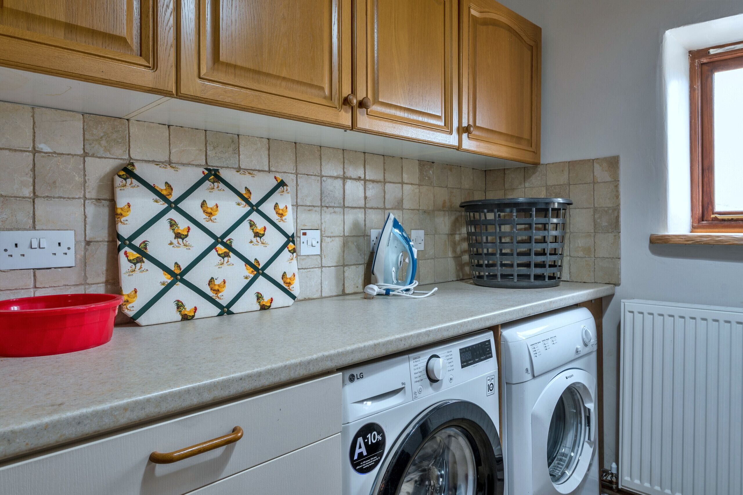 Une cuisine avec des meubles de rangement en bois, un lave-linge, un saladier rouge et un pare-feu en carreaux décoratifs.