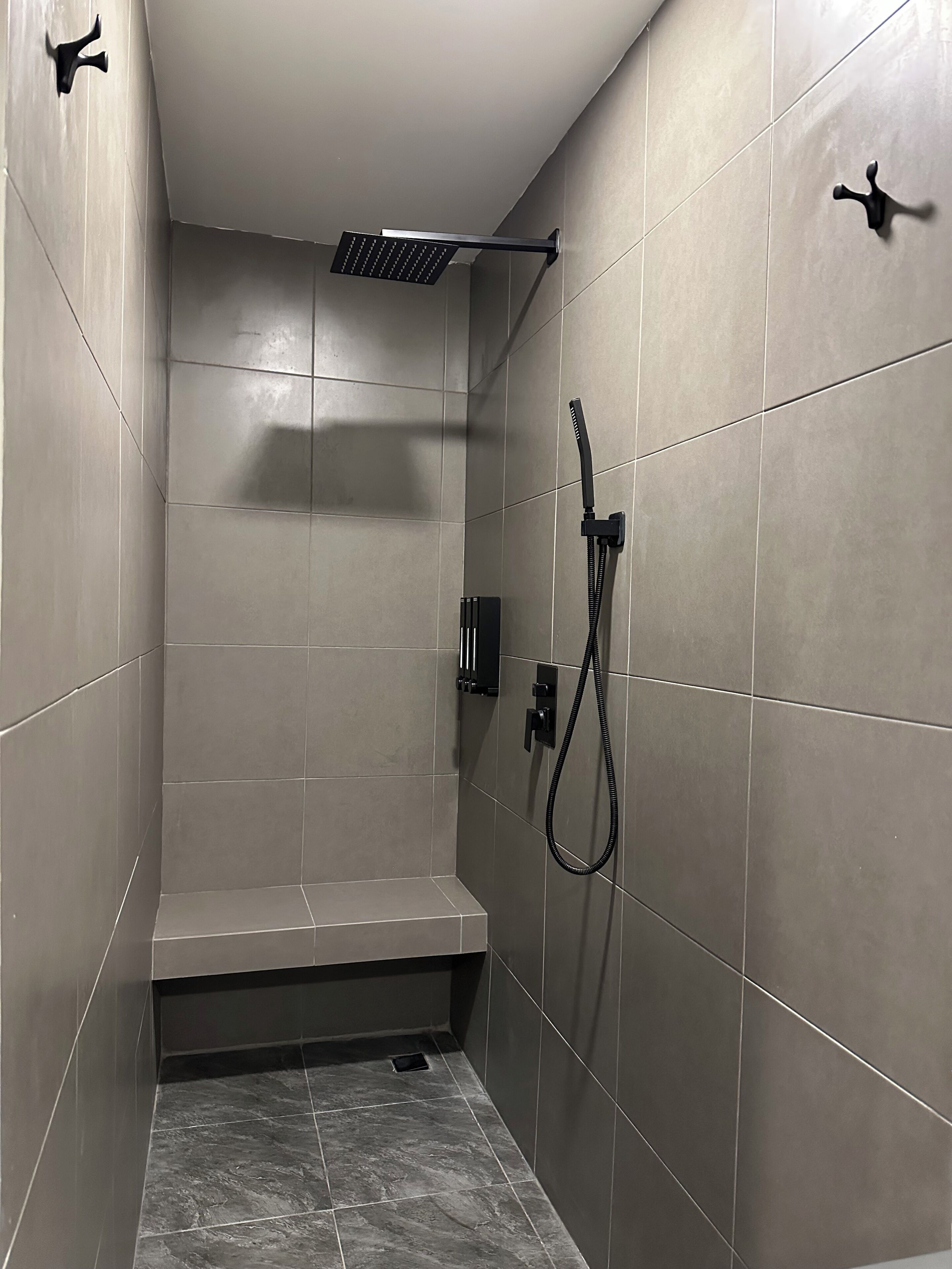 Un área de ducha moderna con un banco, un cabezal de ducha manual y un panel de control en la pared.