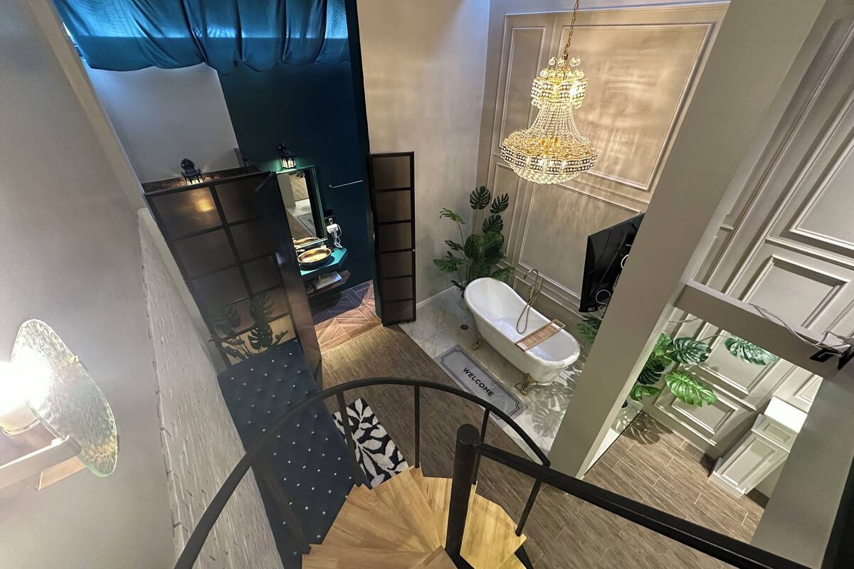 A modern bathroom with a freestanding bathtub, a chandelier, and a large window.