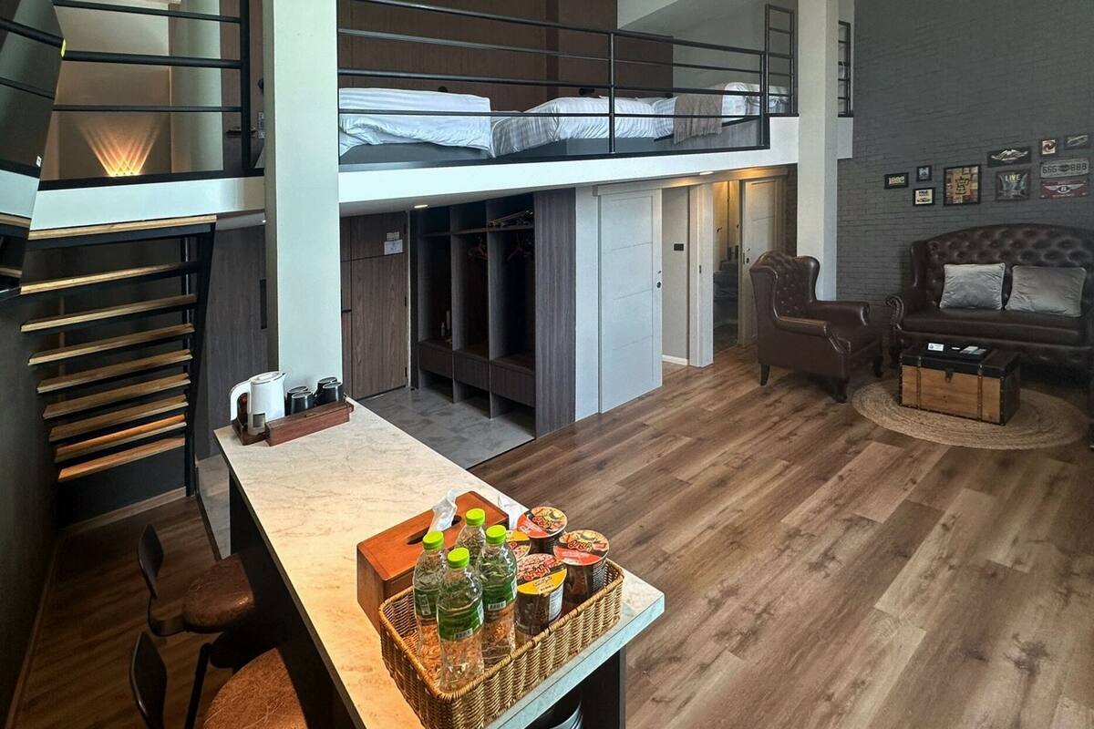 A loft-style bedroom with a bunk bed, a desk with a basket of snacks, and a leather armchair.