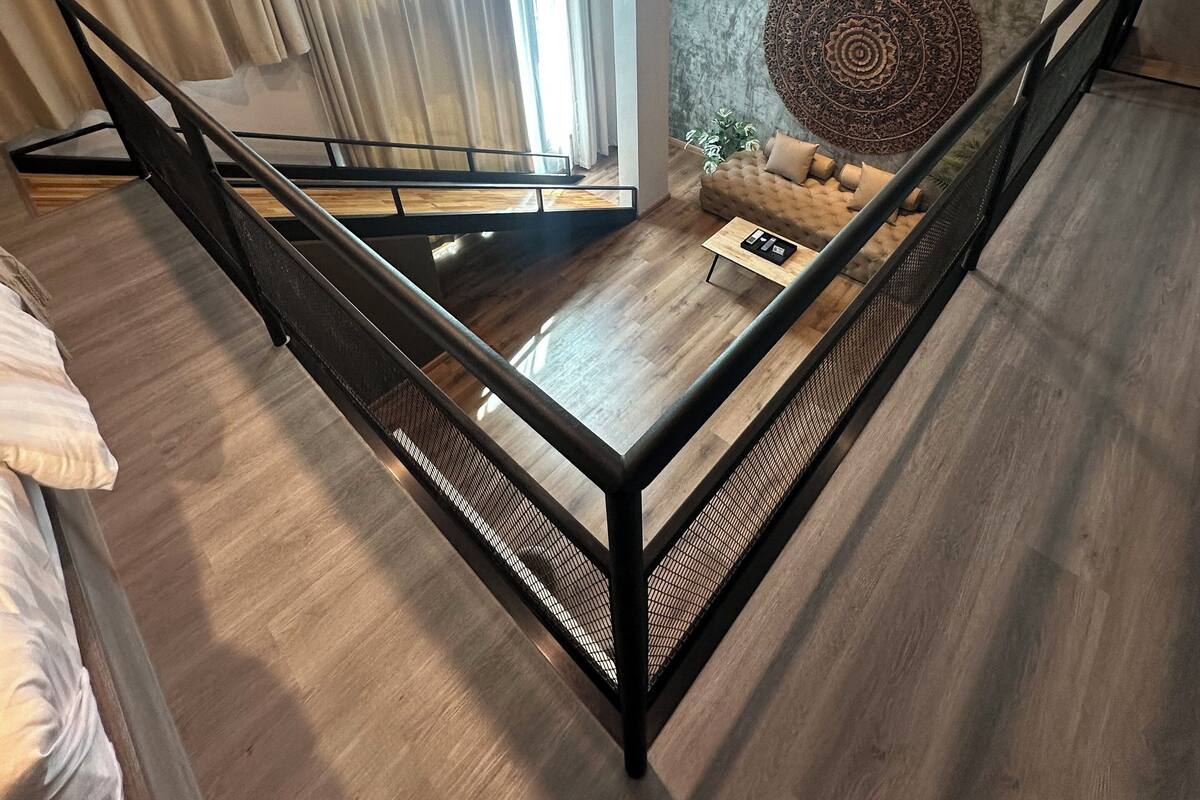 A modern living room with a wooden floor, a sofa, a coffee table, and a decorative wall piece. There is a staircase with a metal railing leading to an upper level.