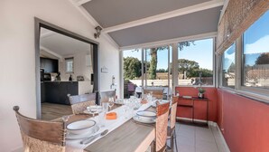 A dining area with a long table set for six, a kitchen in the background, and a view of the outdoors. - 500 m from the beach, garden, 4 adults 1 child (Saint-Michel-Chef-Chef)
