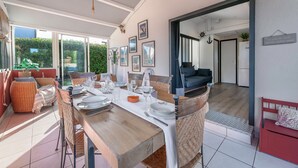A dining area with a wooden table set for four, surrounded by wicker chairs, and a view of the garden through large sliding doors. - 500 m from the beach, garden, 4 adults 1 child (Saint-Michel-Chef-Chef)