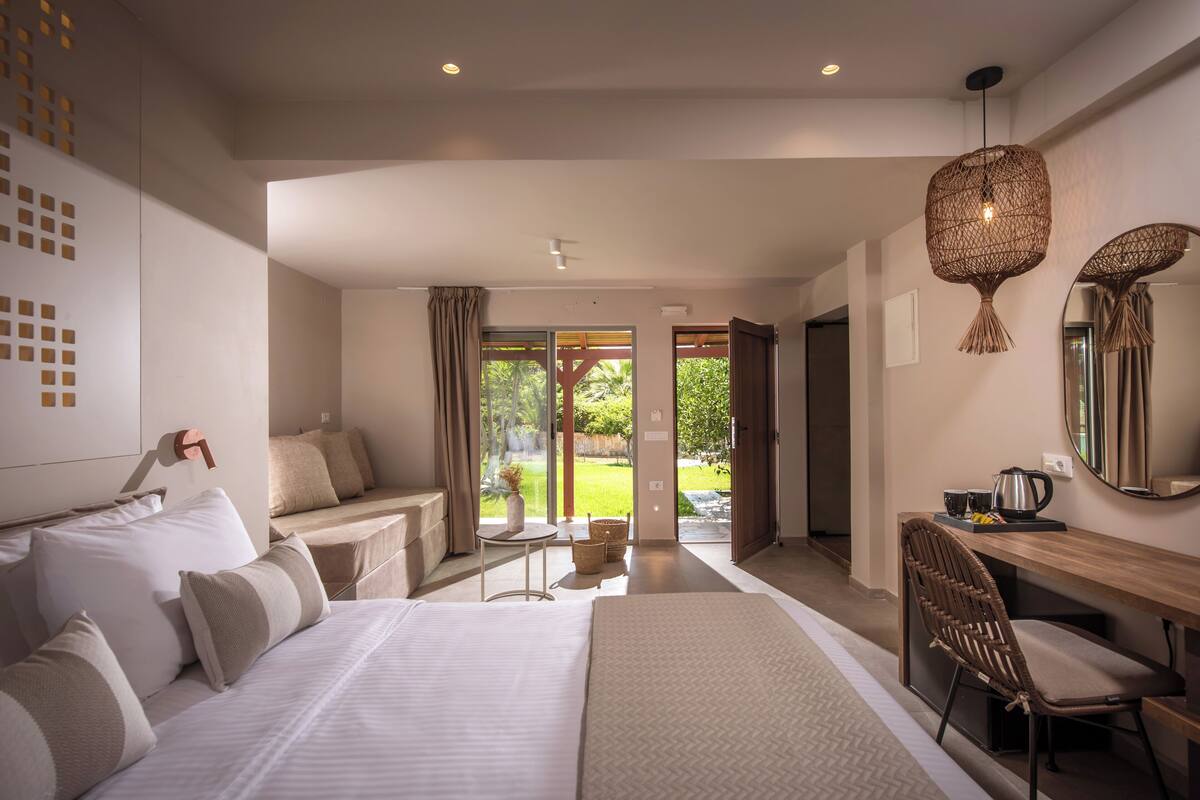 Un hotel moderno con una cama grande, un escritorio, una silla y vista al jardín a través de la puerta de vidrio.