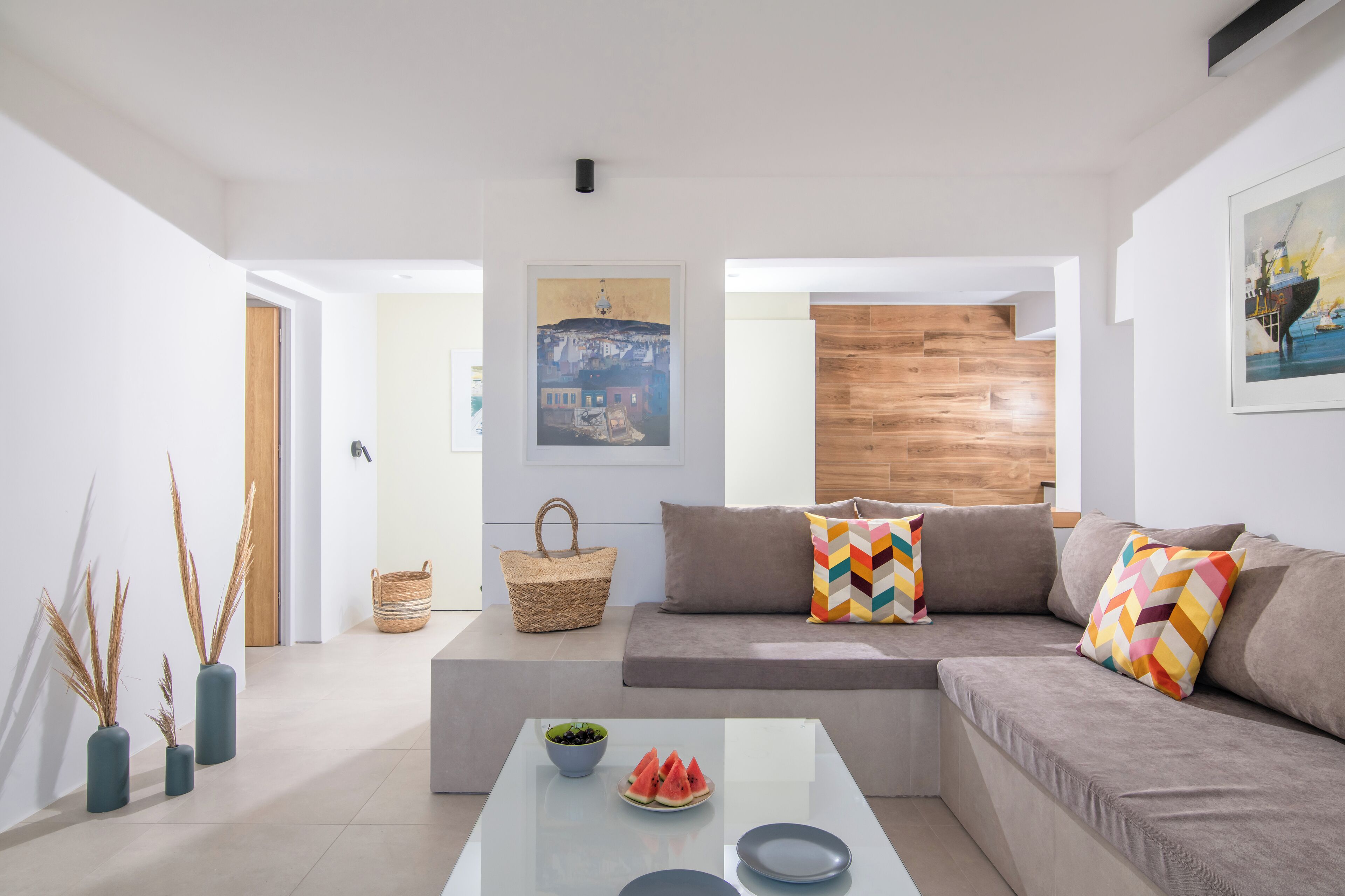 Uma sala de estar moderna com um sofá cinzento, uma mesa de centro com uma tigela e melancia, e uma parede de madeira.