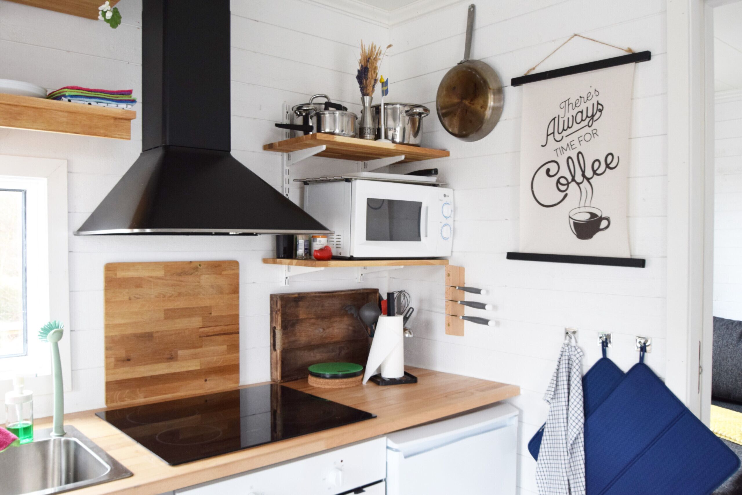 Cozinha moderna com coifa preta, micro-ondas branco e prateleiras de madeira.