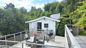Une terrasse en bois avec des meubles d ’extérieur, un barbecue et un petit bâtiment blanc doté d’une fenêtre et d’une porte.