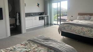 A hotel room with a bed, a sofa, a kitchenette, and a balcony with a view. - A Private Resort in Mangawhai Heads (Mangawhai)