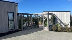 A modern building with a concrete pathway leading to a covered entrance area. - A Private Resort in Mangawhai Heads (Mangawhai)