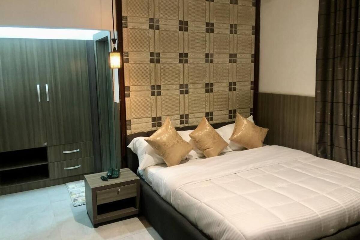 A bedroom with a bed, bedside table, wardrobe, and a patterned headboard.