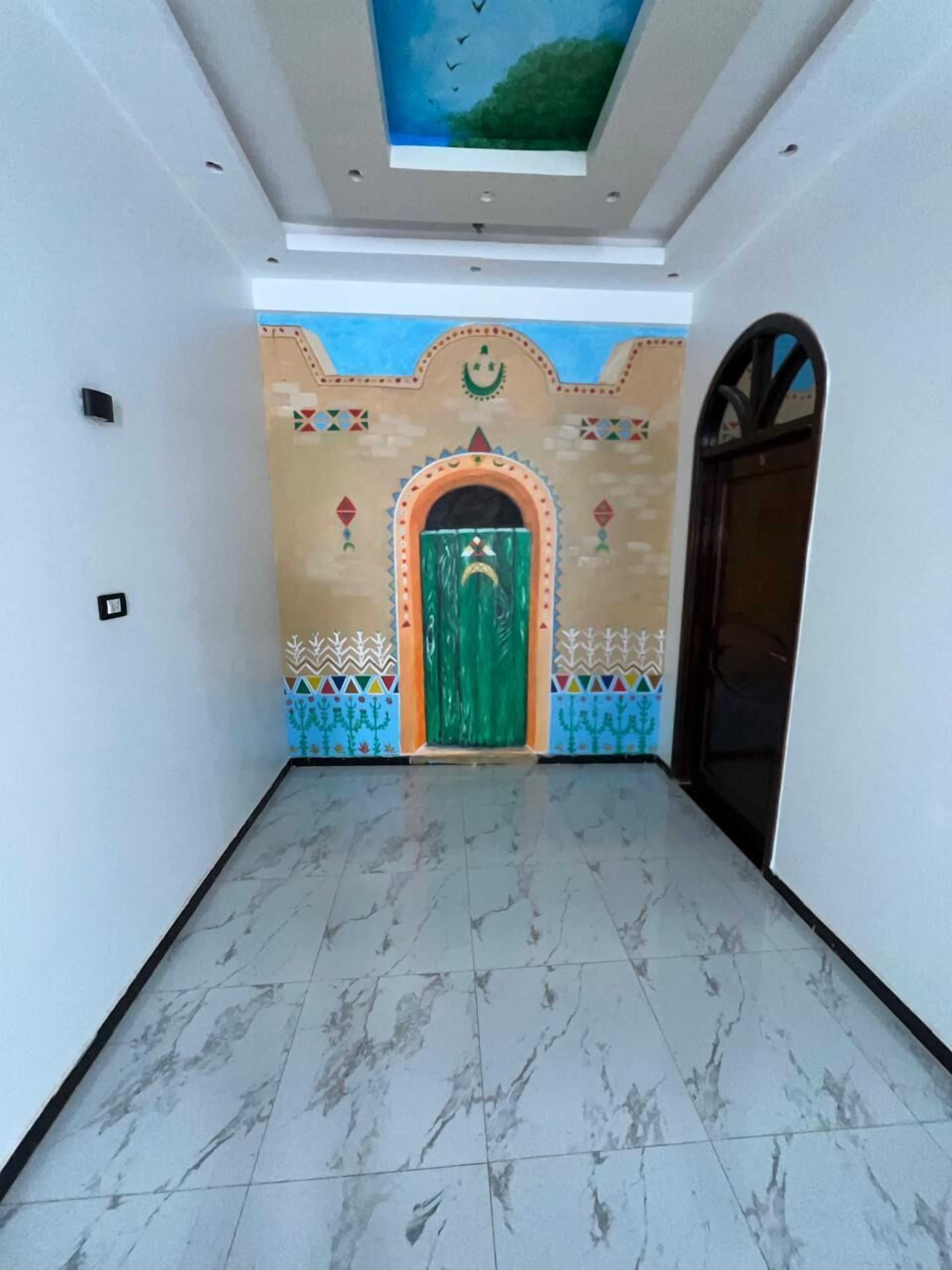 A hallway with a green door, patterned walls, and a tiled floor.