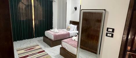 A hotel room with two beds, a ceiling fan, a large mirror, and a striped rug.