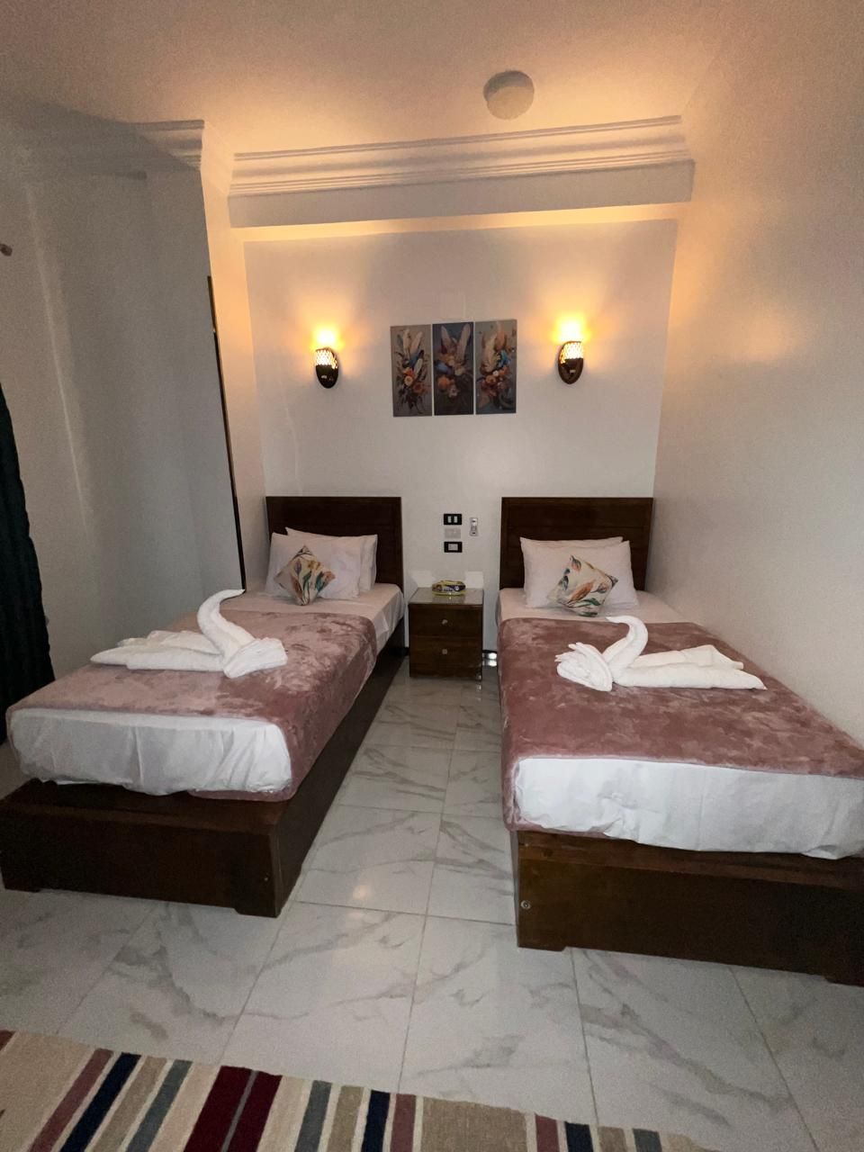 Ein Hotelzimmer mit zwei Betten, einem Marmorboden und einem Streifen Teppich.