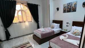 Ein Hotelzimmer mit zwei Betten, einem Fenster mit Vorhängen, einem Deckenventilator und Bildern an der Wand.