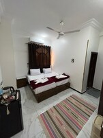 Un dormitorio con cama, ventilador de techo, ventana con cortinas, mesita de noche y alfombra a rayas.
