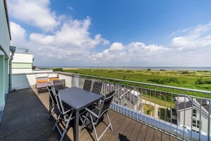 A balcony with a table and chairs, overlooking a green landscape and a body of water.