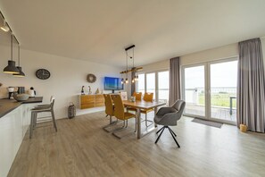 A modern kitchen with a dining area, a TV, and large windows.