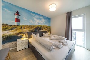 A hotel room with a bed, a nightstand, a lamp, a large window, and a mural of a lighthouse.
