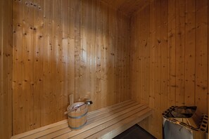 A wooden sauna with benches, a bucket, and a metal container.