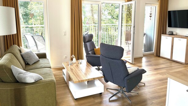 A modern living room with a sofa, a dining table, and a TV. - North Sea apartment with sauna & south-facing balcony - sea breeze and beach just 200 m away (Nordseeheilbad Schillig)