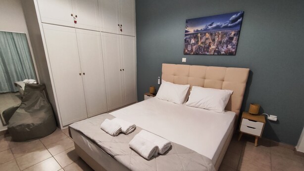 Une chambre à coucher comprenant un lit, une tête de lit, une table de chevet, une commode, un fauteuil en forme de poire et une armoire.