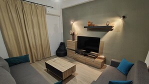 Un salon moderne comprenant deux canapés, une table basse, un téléviseur et une étagère murale agrémentée d’objets décoratifs.