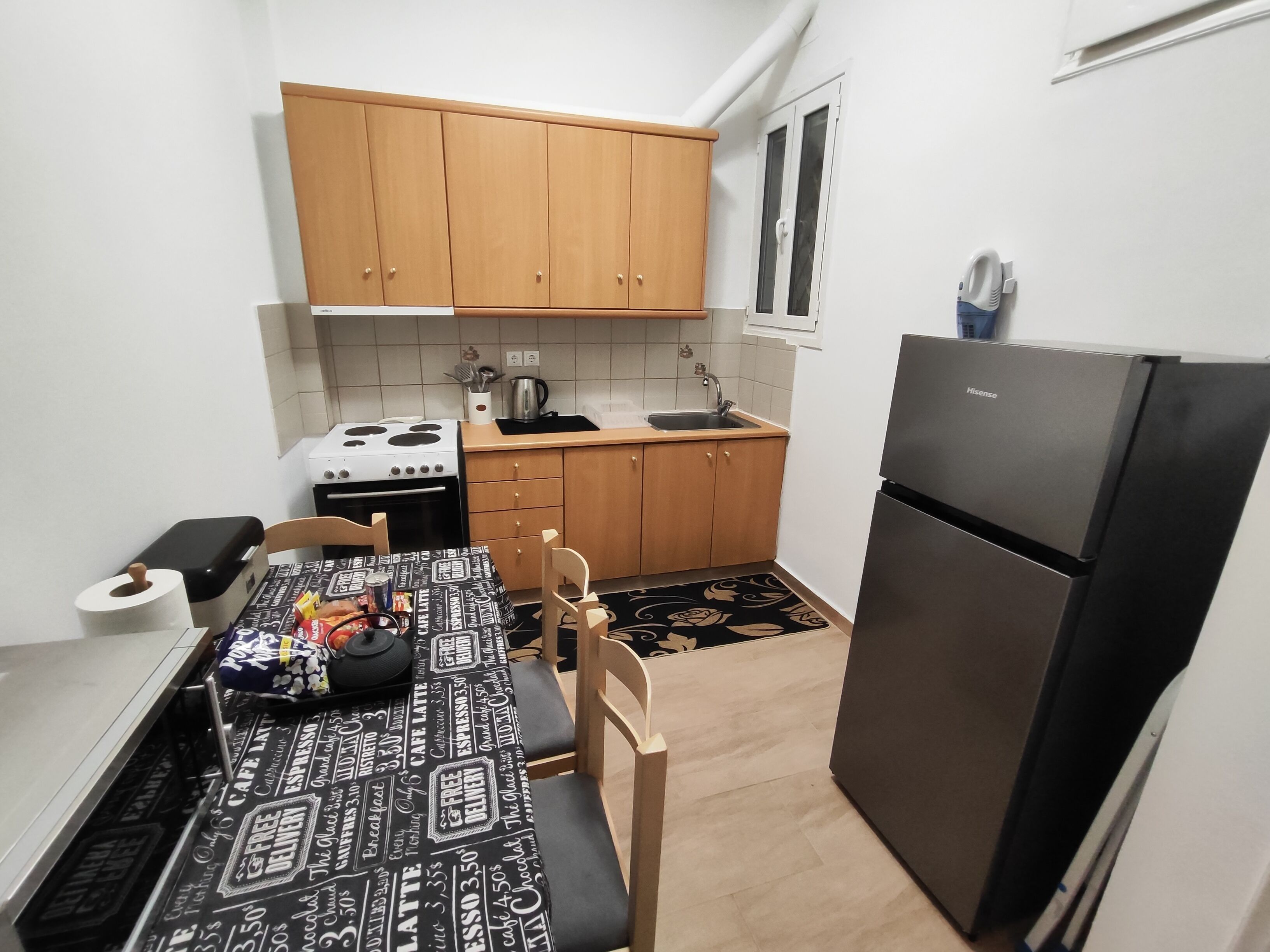 A compact kitchen with wooden cabinets, a black refrigerator, a stove, and a dining table with a black and white patterned tablecloth.