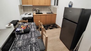 Une cuisine de taille réduite, avec des meubles en bois, un réfrigérateur noir, une cuisinière et une table à manger recouverte d’une nappe à motifs noir et blanc.