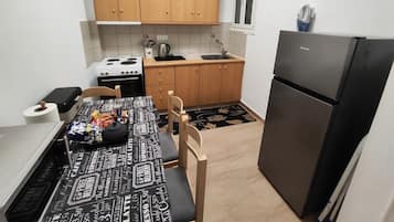 A compact kitchen with wooden cabinets, a black refrigerator, a stove, and a dining table with a black and white patterned tablecloth.