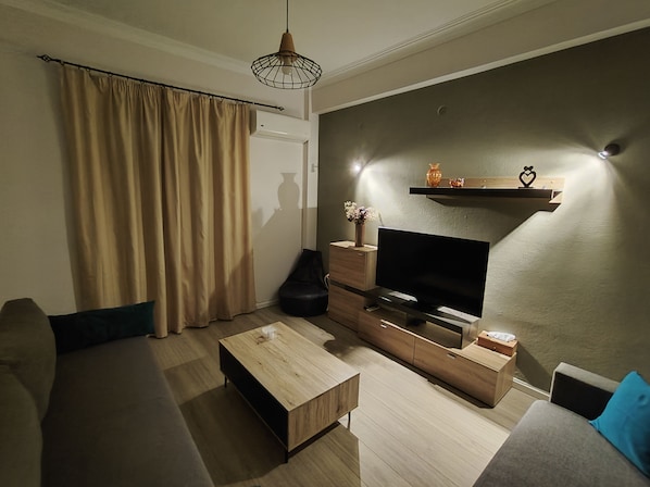 Una sala moderna con una televisión de pantalla plana, muebles de madera, un sofá, una mesa de centro y un estante decorativo.