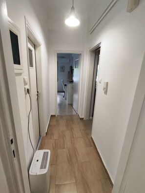 Un pasillo con pared blanca, una lámpara en el techo y un purificador de aire blanco sobre el suelo.