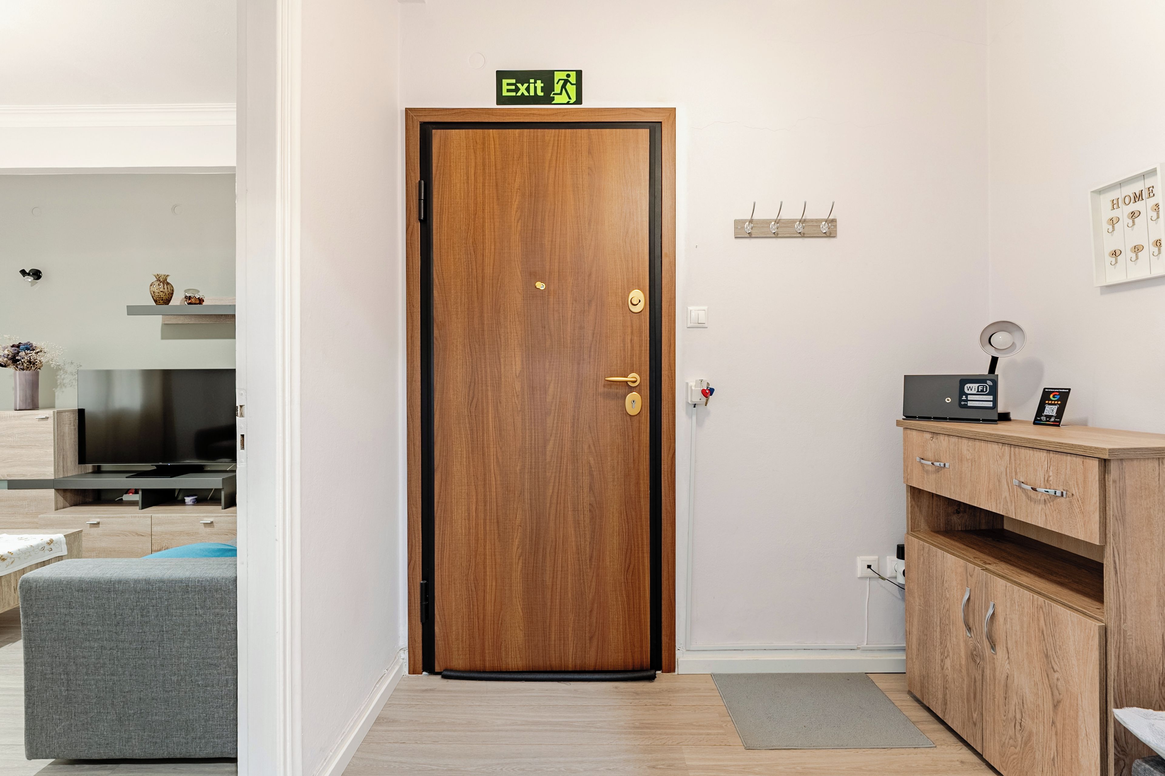 A wooden door with an exit sign, a television, a sofa, a wooden cabinet, and a wall-mounted light fixture.